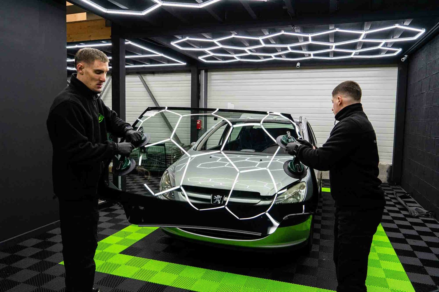 Deux techniciens Pare-Brise Éco posent un pare-brise neuf sur une Peugeot dans un centre du réseau